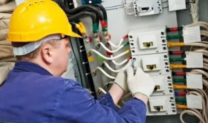 a commercial electrician wearing a yellow hard hat repairing an industrial electrical panel
